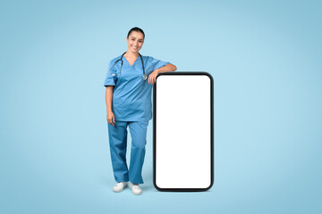 Smiling female nurse in blue scrubs leaning on large blank mobile screen