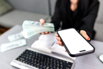 A woman's hand holds a black mobile phone with a white screen on an isolated background and money. Concept of financial services and modern technologies. Finance, transfers, banking services.