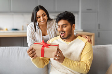 Pleasant Surprise. Loving indian woman giving gift to her husband at home