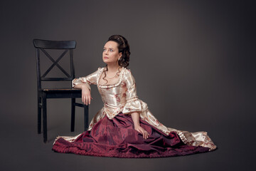 Young beautiful serious woman in medieval style dress sitting on the floor near chair