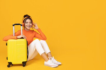 A young girl in headphones and with a yellow suitcase