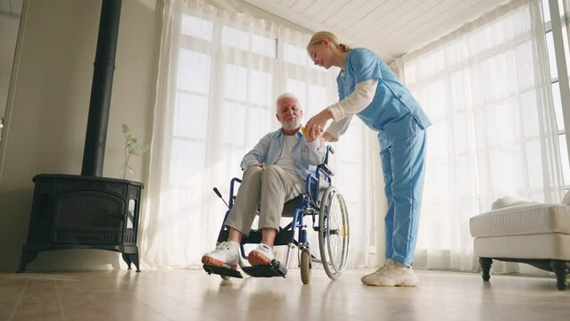 Man in wheelchair exercising with nurse. Social medical worker woman helping senior male doing physical hands exercises with dumbbell. Palliative care in late stage of neurodegenerative pathologies.