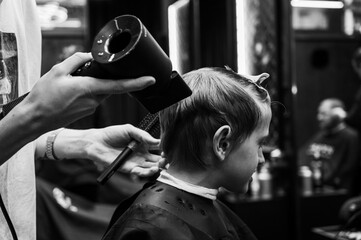 Black and white photo. Cute emotional fair-haired smiling boy with blue eyes at the barber shop....