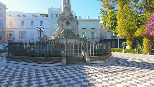 Monumental statue in a plaza with green trees Monument to the Marquis de Comillas in C&aacute;diz, Spain.