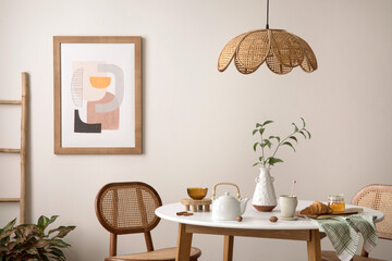 The stylish dining room with round table, rattan chair, wooden commode, pock up poster and kitchen...