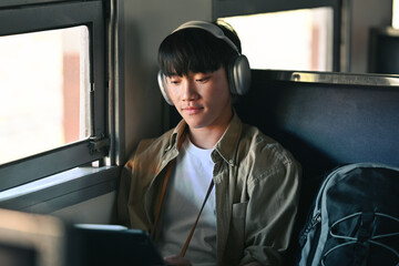 Young man in headphone using digital tablet while commuting by train. Travel and transportation...