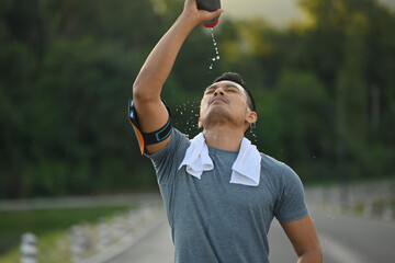 Sporty man pouring water over his face to refresh after after training hard outdoor