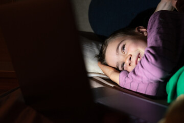 Boy watching a movie on the computer lying in bed at night