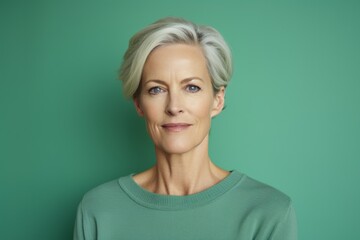 Portrait of beautiful senior woman looking at camera while standing against green background