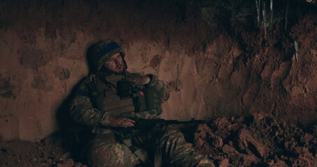 A Urain soldier sits on the bare ground in a dugout with a rosary in his hands and prays. Ukraine's war with Russia.