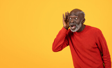 Shocked senior Black man in red sweater, hand to ear, listening intently