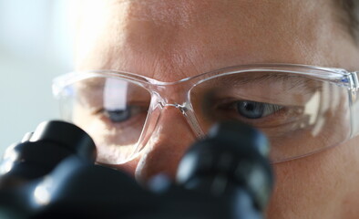 Handsome man scientist looking through binocular microscope examining diseases of the virus that...