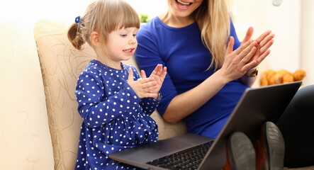 Cute little girl on couch with mom use laptop pc for chat with her dad away on business portrait. Point finger hand in display social web network bank mortgage credit wireless ip telephony concept - obrazy, fototapety, plakaty