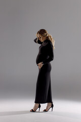 full length shot of loving pregnant woman looking at belly while posing in studio.