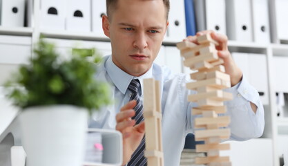 Businessman plays in strategy hand rearranging wooden blocks involved during break at work in...