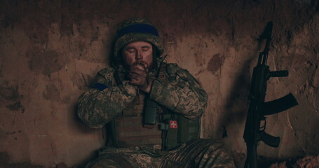 A Urain soldier sits on the bare ground in a dugout with a rosary in his hands and prays. Ukraine's war with Russia.