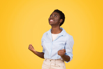 Happy teen black lady student, exuding triumph and joy, raises fists in victorious gesture