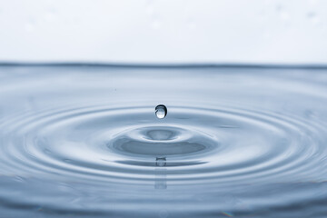 Captivating water droplet in motion, creating ripples on a pristine white background. Ideal for...
