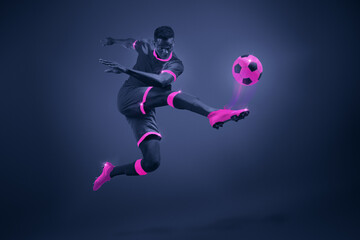 Fototapeta na wymiar African young man, soccer player in mid-kick with selective purple coloring, illustrating movement and focus. Dynamic image of athlete during championship. Poster for sport events, game