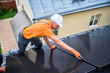 Worker building solar panel system on rooftop of house. Man engineer in helmet and gloves...