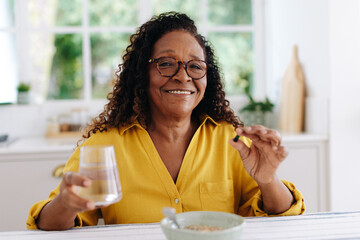 Happy woman adding vitamin supplements to her diet at breakfast