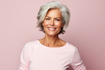 Mature woman with grey hair. Portrait of beautiful mature woman looking at camera and smiling while standing against pink background - obrazy, fototapety, plakaty