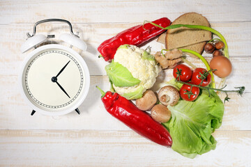Interval fasting or IF, food products, and an alarm clock indicate the period of time during which...