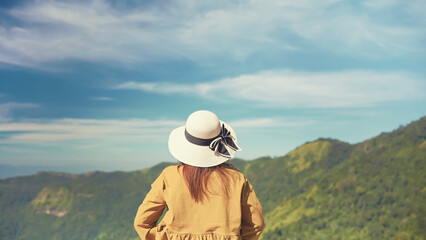 Back view of young woman traveler standing alone while looking beautiful mountain view on sunny day. Travel nature concept