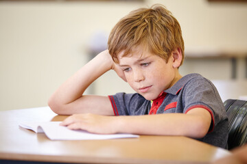 Naklejka premium Class, book and bored child at desk, learning and education with school exam. Reading notebook, studying for test and boy student in classroom with knowledge and thinking with depression on project.