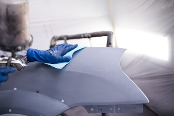 Car paint shop in a car service place. Close up photo of a male hand working to polish and paint the hood of a damaged car. - obrazy, fototapety, plakaty