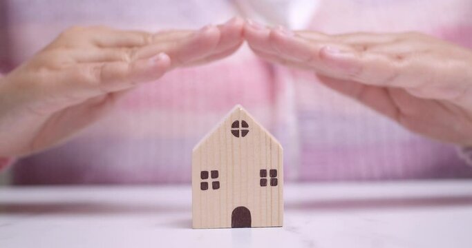 Hands hovering over a tiny wooden house manifesting a desire of owning a house and lot real-estate property.