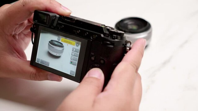 Close-up of an individual holding a point-and-shot digital camera while focusing on a lens on a table and adjusting the aperture and ISO settings.
