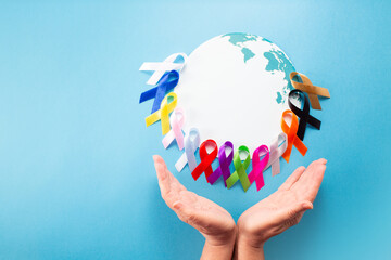 World cancer day February 4. Hand holding colorful awareness ribbons on world map. Healthcare and...
