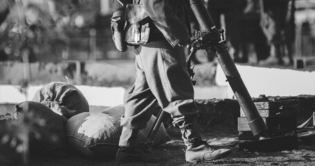 Close-up View On Re-enactor Dressed As German Wehrmacht Infantry Soldier In World War Ii With Submachine Gun Mp 40 Patrols Territory Of Mortar Crew. German Soldier Guards Mortar. Black And White .