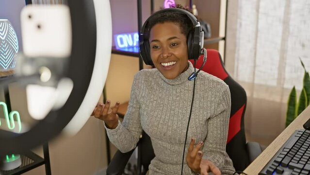 Young woman with curly hair streaming in a gaming room with ring light and headphones, showing mixed race and cheerful expression.