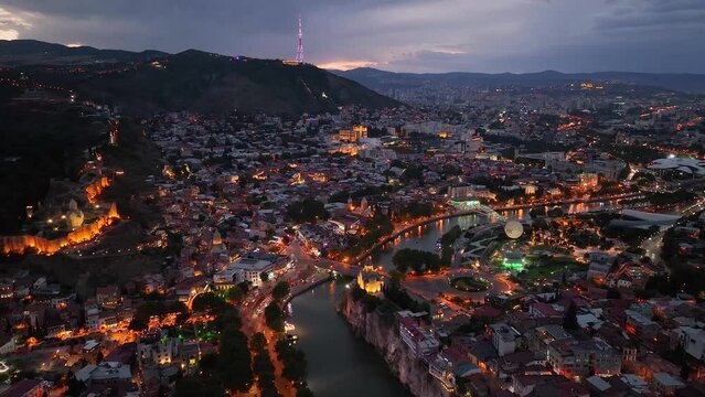 Tbilisi, Georgia. Scenic aerial view at twilight Of Famous Landmarks In Night Illuminations. Cityscape. Overview of the Kura (Mtkvari) River in Old Town, Tbilisi city central park and Bridge of Peace