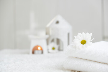 Obraz na płótnie Canvas White towels with chamomile and aroma lamp, candle on background. Spa therapy and wellness, aromatherapy relaxation. Massage salon or beauty salon. Body care and treatment. Self Love. Copy space.