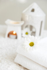 White towels with chamomile and aroma lamp, candle on background. Spa therapy and wellness, aromatherapy relaxation. Massage salon or beauty salon. Body care and treatment. Self Love. Copy space.