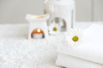Fototapeta na wymiar White towels with chamomile and aroma lamp, candle on background. Spa therapy and wellness, aromatherapy relaxation. Massage salon or beauty salon. Body care and treatment. Self Love. Copy space.
