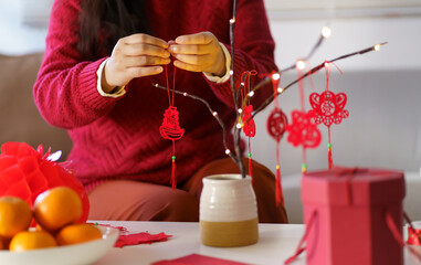 Asian Woman decorated house for Chinese New Year Celebrations. putting traditional pendant to the...