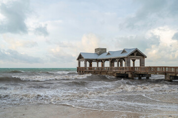 A wooden pier, with a covered portion at the end, reaching out into a choppy, rough sea