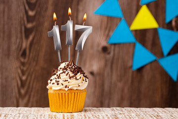 Burning candle - birthday number 117 on wooden background with pennants