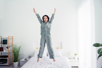 Photo portrait of attractive young woman jump bed raise hands cheerful dressed stylish gray pajama...