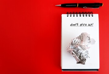 Pen and crumpled paper notebook with text DO NOT GIVE UP on red copy space background, concept of...