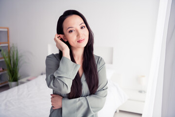 Photo portrait of pretty young girl tuck hair behind ear dressed stylish gray nightwear isolated on comfortable modern white bedroom