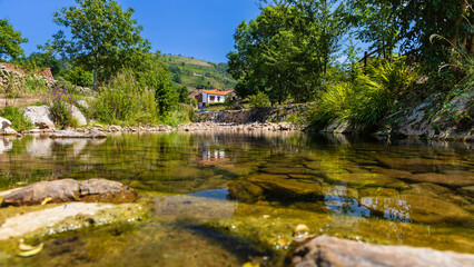 Fototapeta na wymiar Clear river, stones, vegetation, houses. Carmona, Cantabria, Spain.