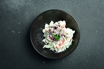 Salad of cabbage, tomatoes, onions and radish dressed with sour cream. On a plate. Restaurant serving. Close up. On a dark stone background.