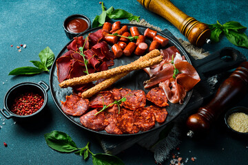 Antipasto plate: prosciutto, salami, pepperoni and grissini. On a dark background, close-up.