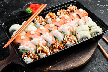 Sushi delivery. Sushi rolls with cheese and fish. Disposable tableware. On a wooden board.