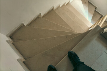 A man in black sneakers begins to descend the steps of the staircase, which spiral in the direction...